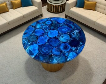 May include: A round blue agate coffee table with a gold base. The table top is made of natural agate stone with a unique pattern of blue and white swirls.