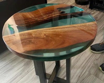 May include: A round wooden table with a green epoxy resin top. The table has a black metal base with a cross-shaped design.