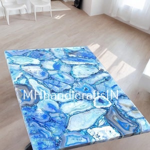Könnte beinhalten: Eine blaue Achat-Tischplatte mit einem schwarzen Metallgestell. Die Tischplatte hat ein einzigartiges Muster aus blauem und weißem Achat. Der Tisch steht in einem Raum mit weißen Wänden und einem hellen Holzboden. Der Text "MHhandicraftsIN" ist auf der Tischplatte sichtbar.