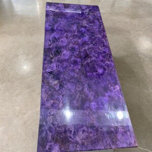Può includere: Tavolino rettangolare in ametista. La superficie del tavolo è un mosaico di tonalità viola intenso con sfumature più chiare e motivi naturali. La superficie lucida riflette la luce. Un elemento d'arredo per il soggiorno.