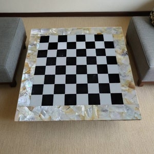 Könnte beinhalten: Ein Schachbrett-Tischplatte in Schwarz und Weiß mit einem Perlmutt-Einlegeband.