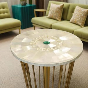 Puede incluir: Una mesa auxiliar redonda con una tapa con incrustaciones de nácar y patas de metal dorado. La parte superior de la mesa presenta una gema verde central y un patrón decorativo. Es un mueble decorativo.