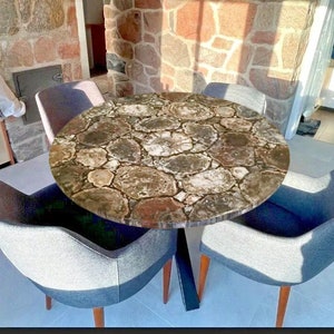 May include: A round dining table with a unique petrified wood top. The table has a black metal base and is surrounded by four gray chairs.