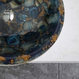 May include: A round, blue and gold sink with a unique agate design. The sink has a drain hole in the center.