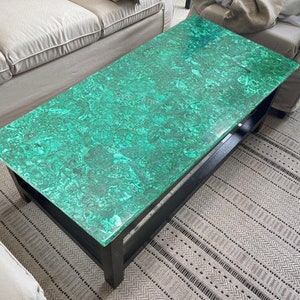 Op de afbeelding: Een zwarte salontafel met een groen malachiet blad. De tafel heeft een eenvoudig ontwerp met één plank.