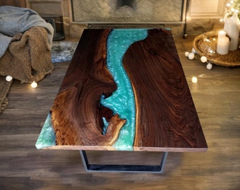 May include: A coffee table with a dark wood top and a turquoise blue resin river running through the center. The table has a black metal base.