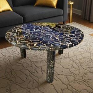 May include: A round coffee table with a blue and gold agate top and three black legs. The table is on a beige rug.