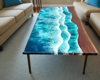 May include: A rectangular coffee table with a unique ocean wave design. The table features a dark wood base with a turquoise and white resin top, mimicking ocean waves. The table has four dark metal legs.