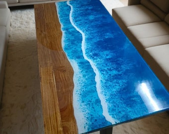 May include: A wooden coffee table with a blue and white epoxy resin top that resembles ocean waves. The table has a black metal leg.