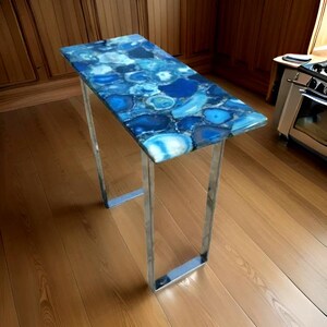 May include: A modern console table with a blue agate top and a chrome metal frame. The table is standing on a wooden floor.