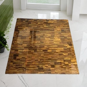 May include: A brown and gold tiger's eye rug with a geometric pattern. The rug is made of small, rectangular pieces of tiger's eye stone.