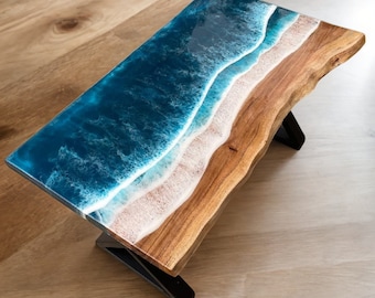 May include: A wooden coffee table with a blue and white epoxy resin top that resembles ocean waves. The table has a natural wood edge and black metal legs.