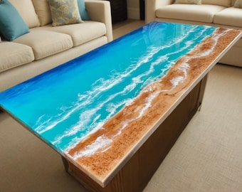 May include: A rectangular coffee table with a resin top depicting a beach scene. The top features a gradient of blue and turquoise representing the ocean, with white wave details and a brown, sandy beach edge.