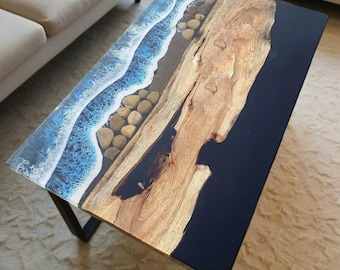 May include: Rectangular coffee table with a unique design. The table features a section with a blue and white ocean wave design, a section of natural wood, and a black resin section. The table is supported by black metal legs.