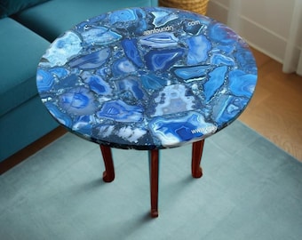 May include: Round side table with a blue agate stone top. The table has three wooden legs and a dark blue rim. The agate stone top features shades of blue and white. The table is placed on a blue rug.