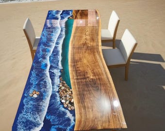 May include: A unique dining table with a live edge design. The table features a blue epoxy resin design that mimics ocean waves, with a section of natural wood grain. The table is surrounded by three white chairs.