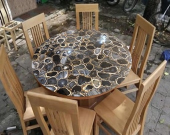 Könnte beinhalten: Ein runder Esstisch mit einer Tischplatte aus schwarzem und goldenem Achat. Der Tisch ist von sechs Holzstühlen umgeben.