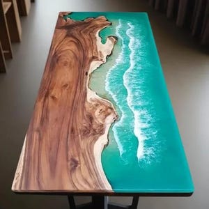 May include: A rectangular wooden table with a unique design. The table features a natural wood grain on one side and a turquoise resin design resembling ocean waves on the other. The table's design creates a coastal theme.