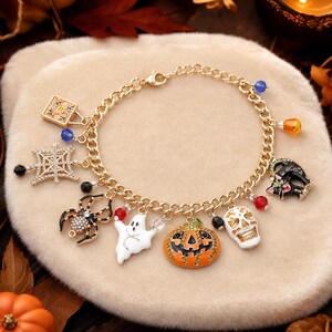 May include: A gold-tone chain link bracelet featuring various Halloween-themed charms including a spider web, a spider, a ghost, a jack-o'-lantern, a skull, and a black cat, accented with small colorful beads and clear crystals throughout the design.