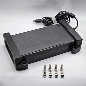 Könnte beinhalten: Ein schwarzes elektronisches Gerät mit gebürsteter Metalloberfläche, rechteckig, mit zwei schwarzen Halterungen. Ein schwarzes Kabel ist mit dem Gerät verbunden. Vier Schrauben und vier Muttern sind ebenfalls enthalten.