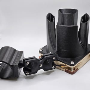 May include: A black 3D-printed device with multiple cylindrical openings and a fan. The device has a complex design with various angles and curves. It is mounted on a beige and brown base with screws.