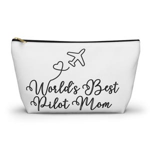 Puede incluir: Bolsa blanca con cremallera con un avión negro y un corazón con el texto "World's Best Pilot Mom" en cursiva negra.