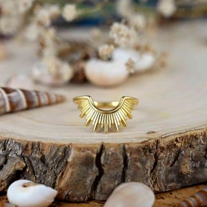 May include: A gold-toned ring with a sunburst design. The ring is open in the back and has a pointed, starburst shape.