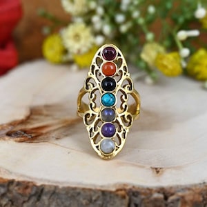 May include: A gold ring with a filigree design and seven colorful gemstones. The gemstones are arranged in a vertical line and represent the seven chakras.