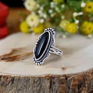May include: A silver ring with an oval black gemstone set in a detailed ornate design.