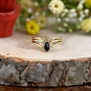 Puede incluir: Anillo de oro con tres bandas que forman una V y una piedra ovalada negra en el centro.