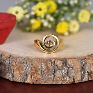 May include: A gold-coloured ring with a spiral design. The ring is on a wooden surface.