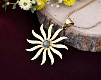 May include: A gold necklace with a sunburst pendant featuring a blue gemstone in the center. The pendant is made of brass and has a detailed design.