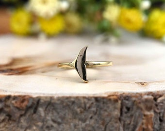May include: A gold-colored ring with a whale tail design. The ring is sitting on a piece of wood.