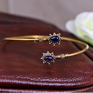 Può includere: Un braccialetto dorato con due accenti di pietre preziose viola. Ogni pietra preziosa è incastonata in un design a forma di stella.