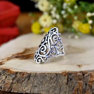 May include: A silver filigree ring with a delicate, intricate design. The ring is made of a single piece of metal and has a wide, open band.