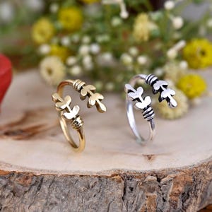 Puede incluir: Dos anillos ajustables con un diseño de hojas. El anillo de la izquierda es dorado y el anillo de la derecha es plateado.