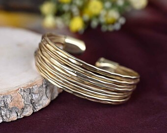 May include: A gold-toned multi-strand bangle bracelet with a hammered finish. The bracelet is made of multiple thin bands of metal that are stacked on top of each other.