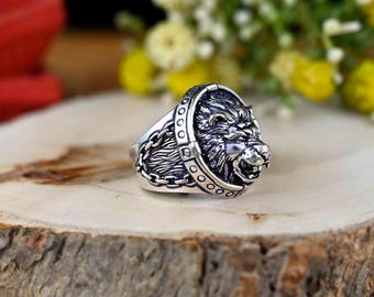 Könnte beinhalten: Ein silberner Ring mit einem detaillierten Wolfskopf-Design. Der Wolfskopf ist von einem Kettengliederrand umgeben.