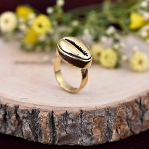Op de afbeelding: Gouden ring met een schelpvormig ontwerp. De ring ligt op een houten oppervlak.