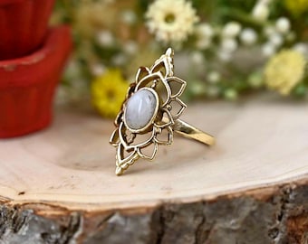 May include: A gold ring with a white gemstone set in a delicate, intricate design. The ring is a statement piece with a bohemian style.