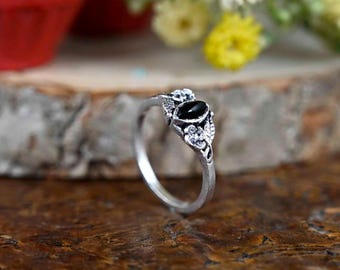 May include: A silver ring with a black oval stone and white accents. The ring is set on a wooden surface.