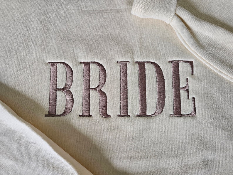 May include: A white sweatshirt with the word "BRIDE" embroidered in brown on the front.