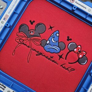 May include: Red fabric with embroidered cartoon character designs, including a mouse head with a bow, a wizard hat, and mouse ears with a bow. The text "Some imagination, huh?" is also embroidered.
