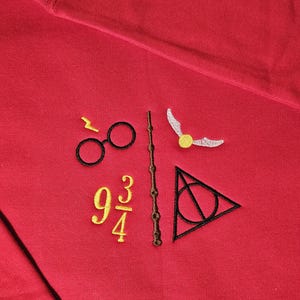 Puede incluir: Sudadera roja con símbolos bordados: gafas, varita, snitch dorada, el número 9 3/4 y un triángulo. Los símbolos son en negro, dorado y blanco.
