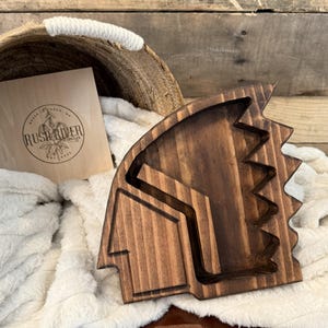 May include: A dark brown wooden tray shaped like a Native American headdress. The tray has a carved design and is perfect for serving snacks or jewelry.