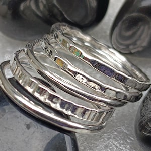 May include: Five silver stacking rings with hammered and textured finishes. The rings are stacked on top of each other and are arranged in a spiral pattern.