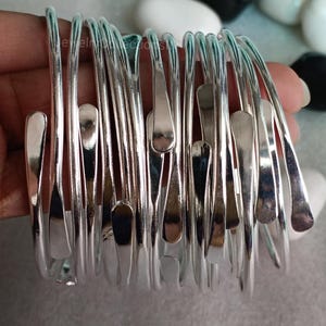 May include: A stack of silver bangle bracelets with a hammered finish. The bracelets are all the same size and shape, and they are arranged in a neat pile.