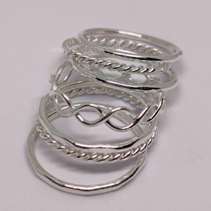 Könnte beinhalten: Ein Set aus sechs silbernen Ringen mit verschiedenen Designs, darunter ein Seil-Design, ein Wellen-Design und ein Unendlichkeits-Symbol-Design.