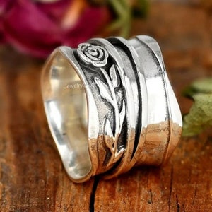 Könnte beinhalten: Ein silberner Drehring mit einem Rosen- und Blätterdesign. Der Ring besteht aus mehreren Bändern, die sich umeinander drehen.