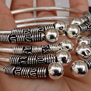 May include: A set of five silver bangles with intricate designs and round beads. The bangles are stacked on top of each other and have a shiny finish.